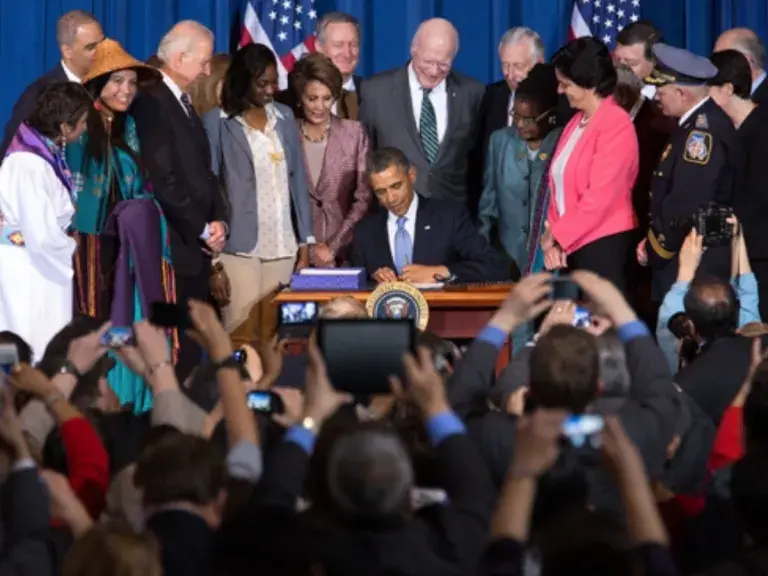 The image shows a large group of people, including some in traditional clothing, President Obama and Vice President Joe Biden.