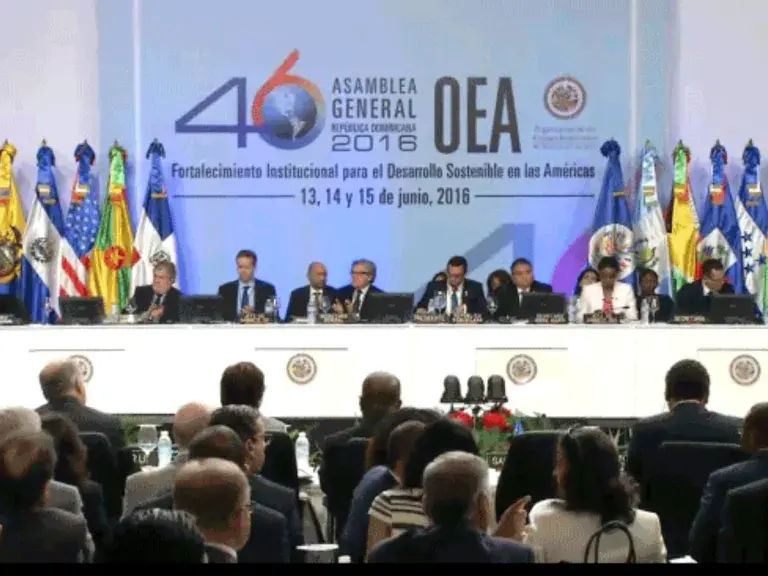 The image shows a group of panelists sitting behind a table in front of a large group.