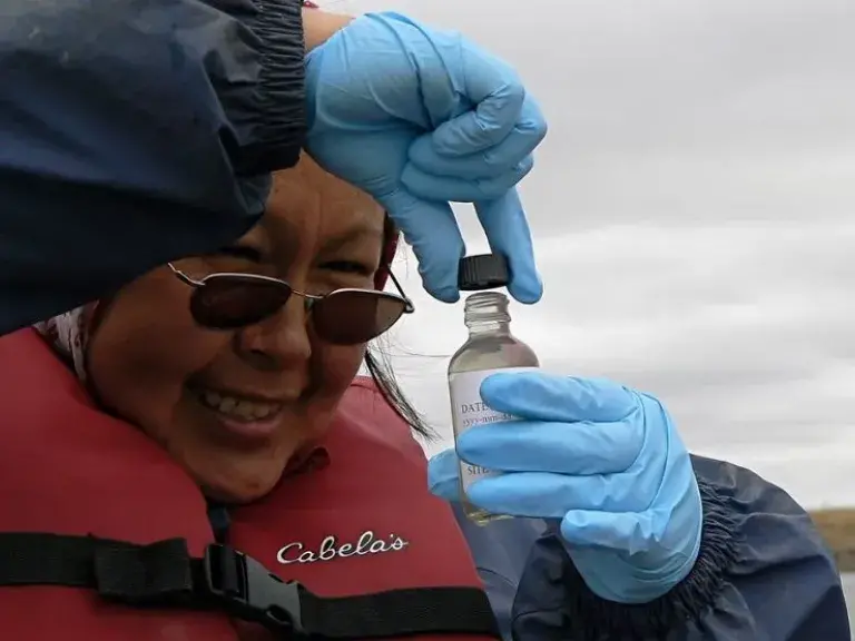 Image shows a women in sunglasses collecting a water sample.
