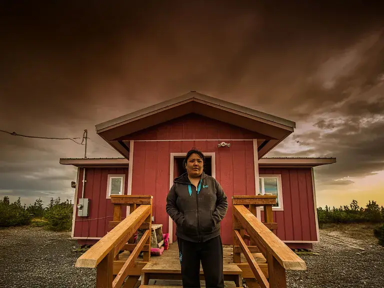native woman standing in front of a red house