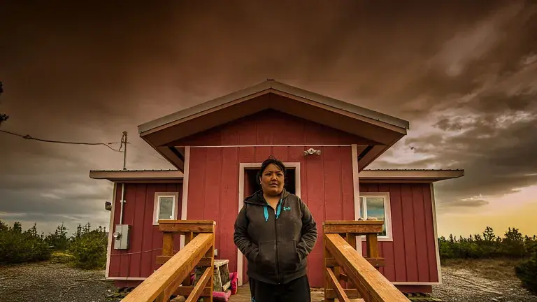 native woman standing in front of a red house